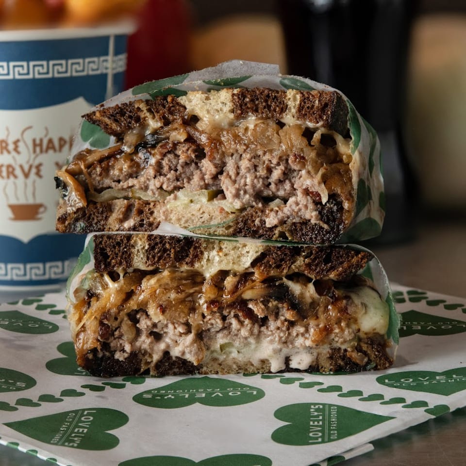 A Lovely's Old Fashioned burger, cut in half, revealing a thick patty, cheese, and caramelized onions.