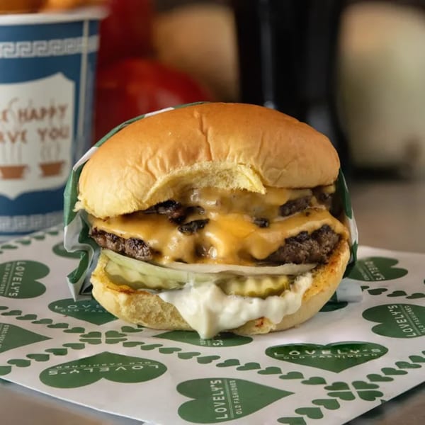 A double cheeseburger from Lovely's Old Fashioned, with melted cheese, pickles, and sauce, on branded paper.