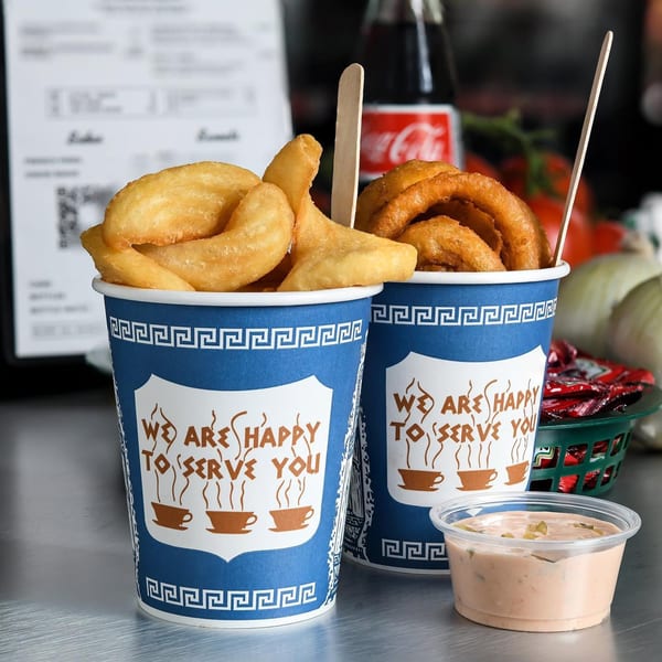 Two blue and white cups of fries and onion rings with a side of dipping sauce.