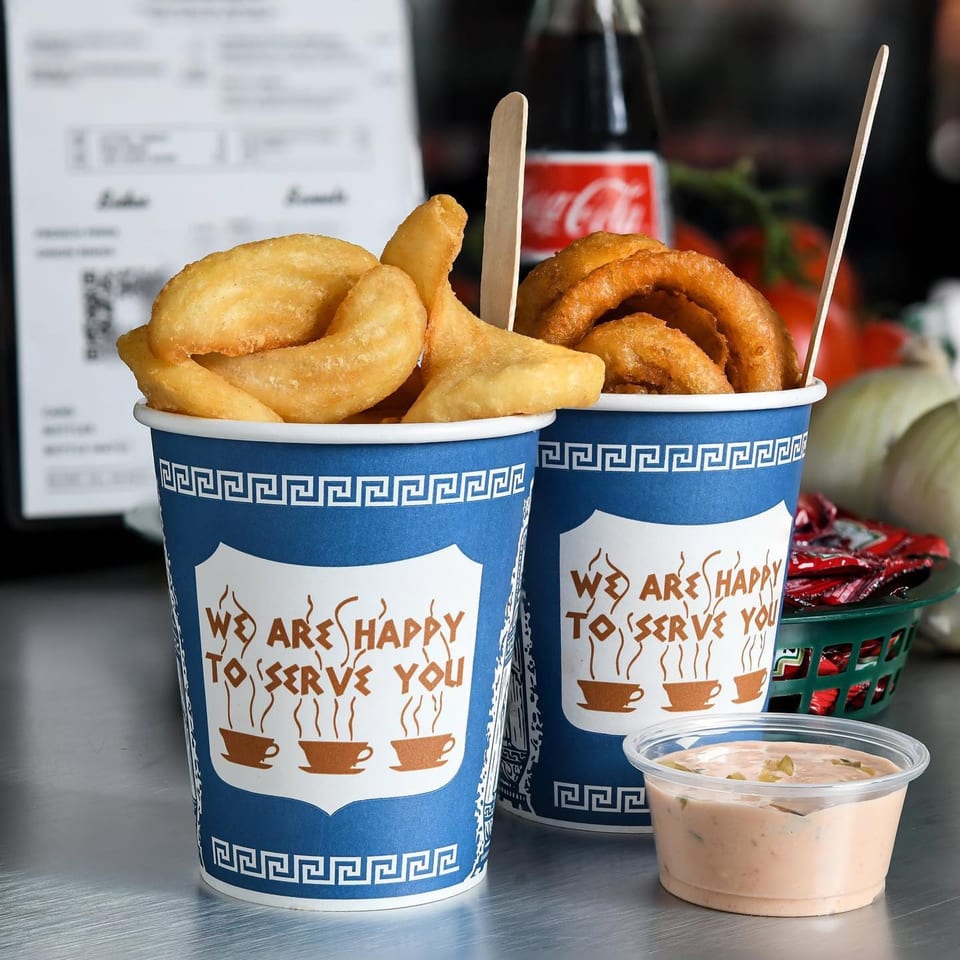 Two blue and white cups of fries and onion rings with a side of dipping sauce.