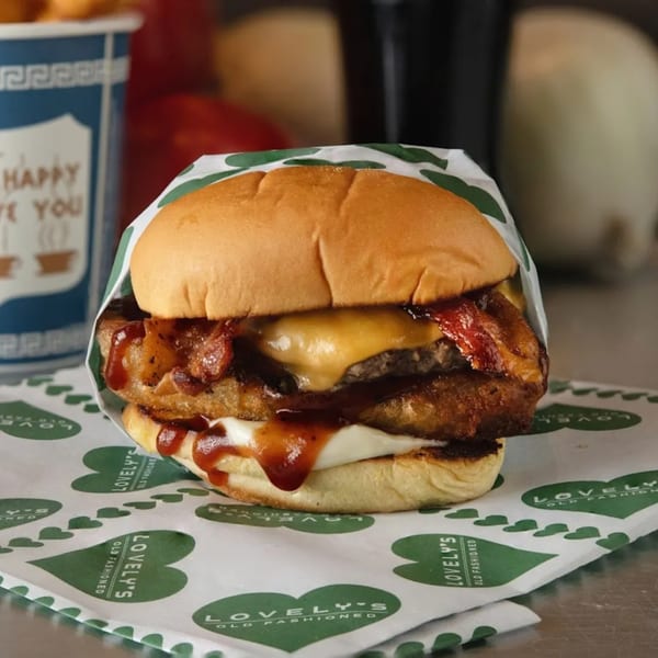 A Lovely's Old Fashioned burger with bacon, cheese, and sauce, wrapped in branded paper.